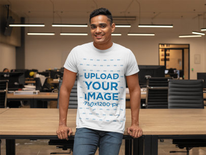T-Shirt Mockup Featuring a Smiling Man Leaning on a Desk at the Office